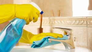 Person cleaning bathroom sink and fixtures with cleaning spray and cloth
