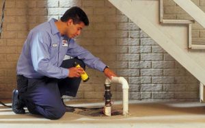 Technician replacing an old sump pump in a basement pit.