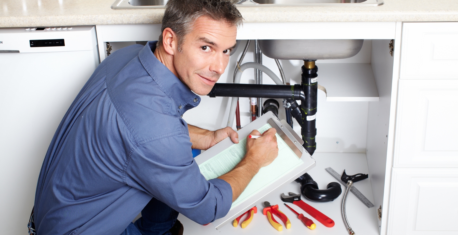 Plumber inspecting a leaking pipe under a kitchen sink.