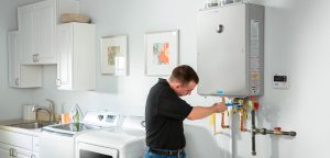 Technician using tools to repair a tankless water heater mounted on a wall.