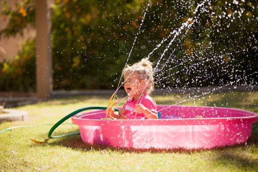 Baby playing with water in a garden bathtub, illustrating backflow prevention and safe outdoor water use.