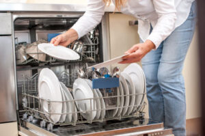 Woman placing kitchen utensils into a dishwasher in a modern home kitchen.