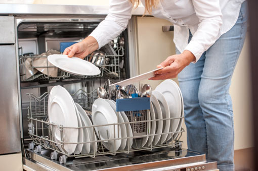Woman placing kitchen utensils into a dishwasher in a modern home kitchen.