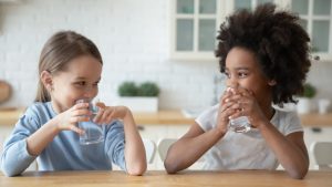 Little multiethnic girls drinking mineral water together at home.