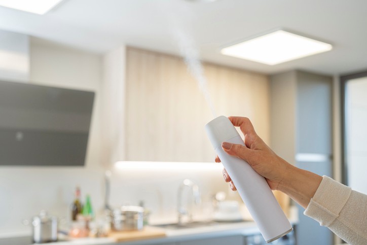 woman's hand spraying air freshener into the air at home