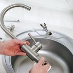 Plumber inspecting kitchen faucet with tape