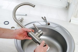Plumber inspecting kitchen faucet with tape